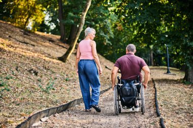 Bir çift, refakatçilik ve kapsayıcılığın altını çizerek, lüks bir parkta sakin bir şekilde yürümekten zevk alır..