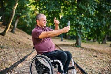Tekerlekli sandalyedeki bir adam yemyeşil bir parkta huzur ve özgürlüğe kucak açan bir yürüyüşün tadını çıkarır..