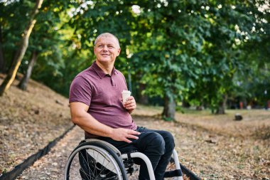 Tekerlekli sandalyedeki bir adam yemyeşil bir parkta huzur ve özgürlüğe kucak açan bir yürüyüşün tadını çıkarır..