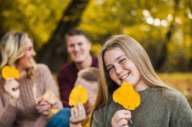 Dört kişilik bir aile, sonbahar parkında yapraklı poz veriyor ve onlarla oynuyor.. 