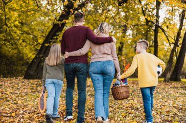Mutlu bir ailenin ellerinde eşyalarla parkta yürümesinin ve güzel bir sonbahar gününün tadını çıkarmasının arka görüntüsü.. 