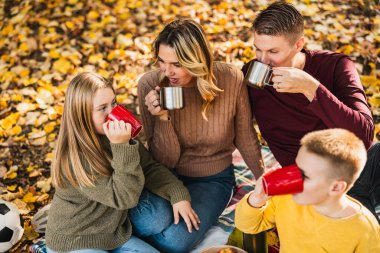 Dört kişilik mutlu ve neşeli bir aile güzel bir sonbahar gününde piknik yaparken parkta güzel bir gün geçiriyor.. 