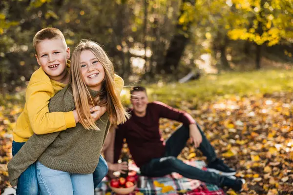 Erkek ve kız kardeş sonbahar günü parkta oynarken ebeveynler onları izliyor.. 