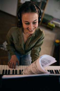 Bir kadın piyanonun başına oturur, notaları dikkatle okur, bir ev ortamında müzik odağı ve yaratıcılığını gösterir..