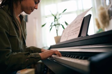 Genç bir kadın nota kağıdıyla piyano çalıyor, odak ve yaratıcılık anı yakalıyor..