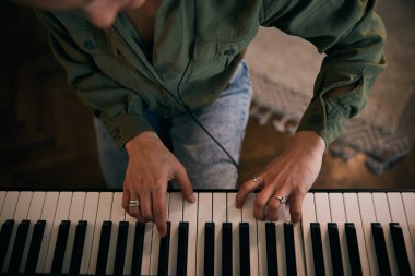 Genç bir kadın nota kağıdıyla piyano çalıyor, odak ve yaratıcılık anı yakalıyor..