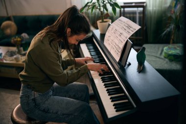 Genç bir kadın nota kağıdıyla piyano çalıyor, odak ve yaratıcılık anı yakalıyor..