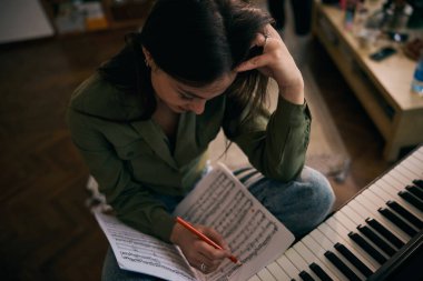 Genç bir kadın evde piyano öğrenirken neşe içinde nota okuyor..