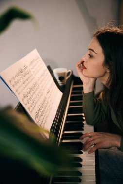 Piyano notaları okumaya derinden odaklanmış genç bir kadın, piyano başında oturuyor.. 