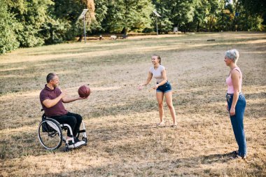 Bir aile, tekerlekli sandalyedeki bir adamla açık havada basketbol oynamaktan zevk alır..