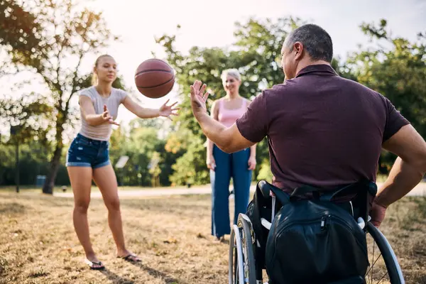 Aile, tekerlekli sandalyedeki adamla basketbol oynarken parkta eğleniyor..