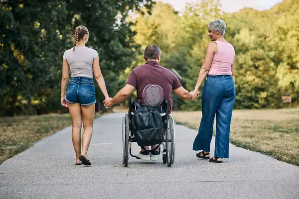 Doğada, tekerlekli sandalyedeki adamlarla yürüyen aile manzarası.. 