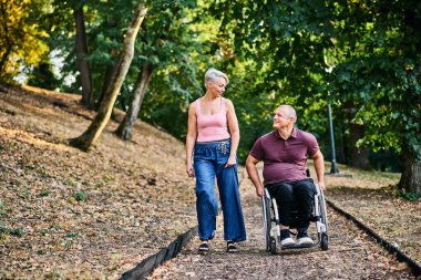 Bir çift, refakatçilik ve kapsayıcılığın altını çizerek, lüks bir parkta sakin bir şekilde yürümekten zevk alır..