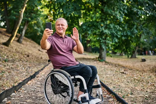 Tekerlekli sandalyedeki bir adam yemyeşil bir parkta huzur ve özgürlüğe kucak açan bir yürüyüşün tadını çıkarır..