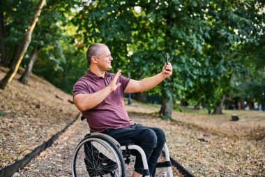 Tekerlekli sandalyedeki bir adam yemyeşil bir parkta huzur ve özgürlüğe kucak açan bir yürüyüşün tadını çıkarır..