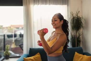 Pembe halterlerle içeride egzersiz yapan kendine güvenen bir kadın.. 