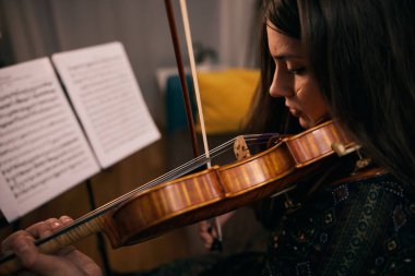 Evde keman çalan kadın oturma odasındaki notalara odaklanmış..
