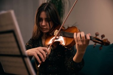 Evde keman çalan kadın oturma odasındaki notalara odaklanmış..