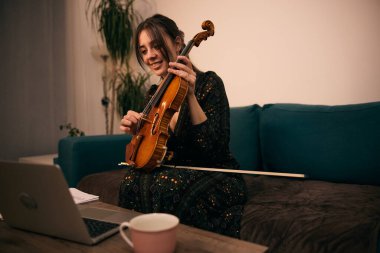 Evde dizüstü bilgisayarında keman dersi alan genç bir kadın.