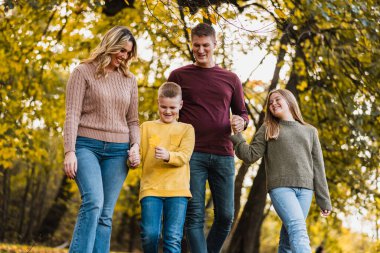 Dört kişilik mutlu bir aile sonbahar günü güzel bir parkta yürüyüş yapıyor.. 