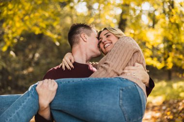 Neşeli bir çift, sonbahar renkleriyle dolu güneşli bir parkta kucaklaşıyor.. 