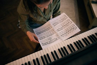 Bir kadın piyanonun başına oturur, notaları dikkatle okur, bir ev ortamında müzik odağı ve yaratıcılığını gösterir..