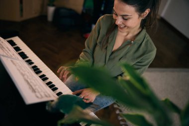 Genç bir kadın nota kağıdıyla piyano çalıyor, odak ve yaratıcılık anı yakalıyor..