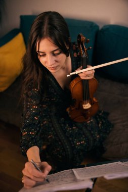 Evde keman çalan kadın oturma odasındaki notalara odaklanmış..
