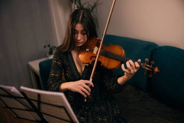 Evde keman çalan kadın oturma odasındaki notalara odaklanmış..