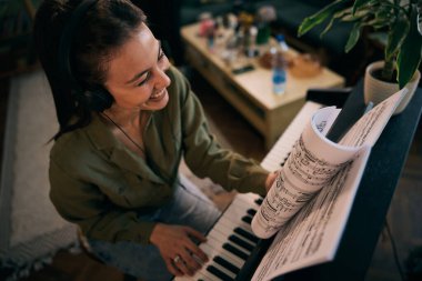 Bir kadın piyanonun başına oturur, notaları dikkatle okur, bir ev ortamında müzik odağı ve yaratıcılığını gösterir..