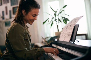 Genç bir kadın nota kağıdıyla piyano çalıyor, odak ve yaratıcılık anı yakalıyor..