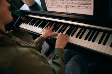 Genç bir kadın nota kağıdıyla piyano çalıyor, odak ve yaratıcılık anı yakalıyor..