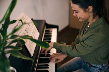 Genç bir kadın nota kağıdıyla piyano çalıyor, odak ve yaratıcılık anı yakalıyor..