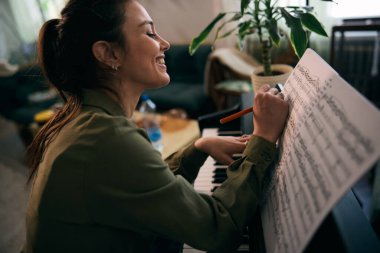 Genç bir kadın nota kağıdıyla piyano çalıyor, odak ve yaratıcılık anı yakalıyor..