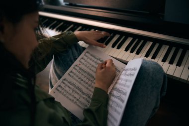 Genç bir kadın evde piyano öğrenirken neşe içinde nota okuyor..