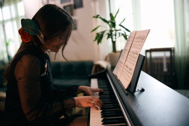 Saçında kırmızı gül olan kadın evde tutkuyla piyano çalıyor..