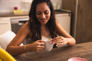 Bir kadın mutfak masasında oturur ve kurabiyelerle kahvenin tadını çıkarır.. 
