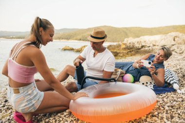 Family enjoying time at rocky beach on sunny day while preparing pool float. 
