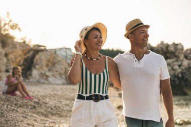 Mutlu ebeveynler sahilde birlikte vakit geçirirken kızları onların arkasında oturuyor.. 