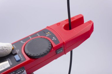 Elektrikçi, faz kablosundaki akımı gri arka plandaki bir metreyle ölçer.