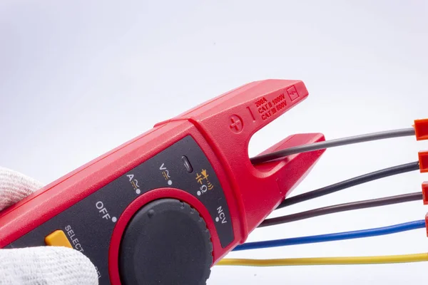 Elektrikçi, faz kablosundaki akımı gri arka plandaki bir metreyle ölçer.