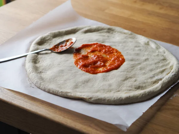 生披萨面团放在木板上 涂酱汁 — 图库照片