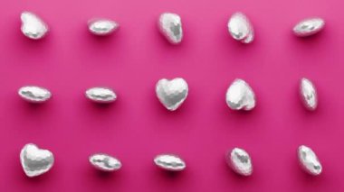 Gelişigüzel dönen gümüş 3D kalp deseni. Sevgililer Günü için aşk konsepti. Pembe arka plan. 4k döngülü animasyon.