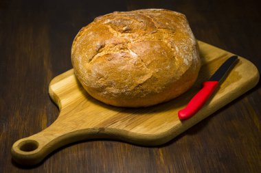 Traditional round loaf of bread on a wooden table - photo of a rustic style in a dark kitchen
