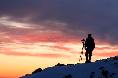 Gün batımında dağlarda tripodla çekim yapan manzara fotoğrafçısı.