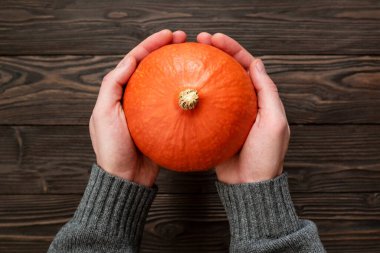 Man Holding an Orange Hokkaido Pumpkin or Uchiki Kuri Squash Over a Wooden Table clipart