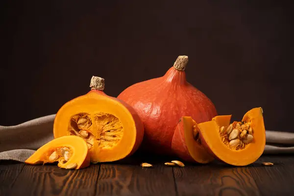 stock image Hokkaido Pumpkins or Red Kuri Winter Squash on a Wooden Table with One Cut into Slices