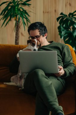 thirty-year-old man with laptop and dog sitting at home on the couch