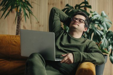 thirty-year-old man with laptop sitting at home on the couch 