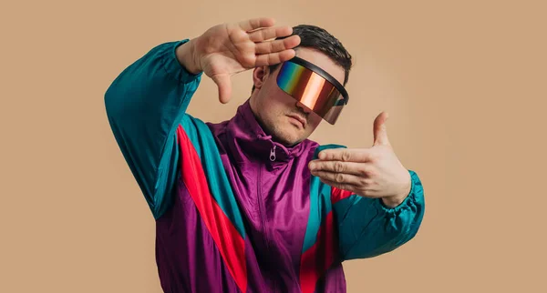 Stylish guy in vintage track suit and VR glasses on brown background